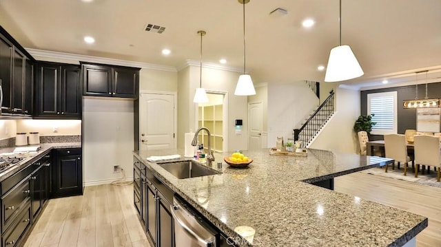 kitchen featuring a center island with sink, decorative light fixtures, dishwasher, light stone counters, and sink