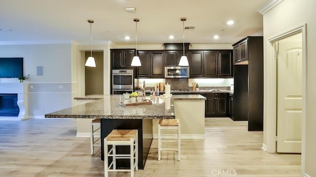 kitchen featuring a kitchen bar, stainless steel appliances, light wood-type flooring, light stone countertops, and pendant lighting