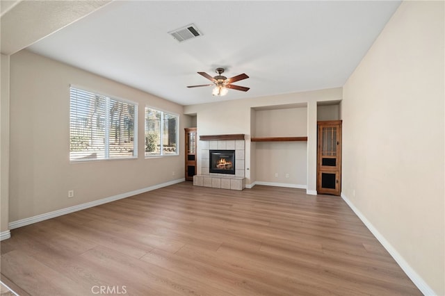 unfurnished living room with ceiling fan, a tile fireplace, and light wood-type flooring