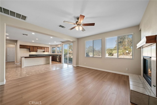 unfurnished living room featuring a tiled fireplace, light hardwood / wood-style flooring, and ceiling fan