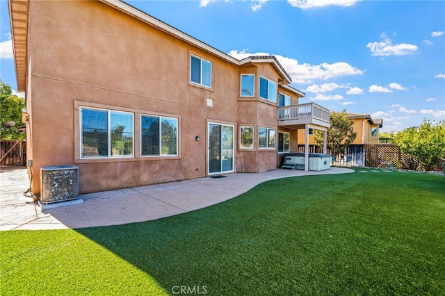 rear view of house with a patio, a balcony, a lawn, cooling unit, and a hot tub