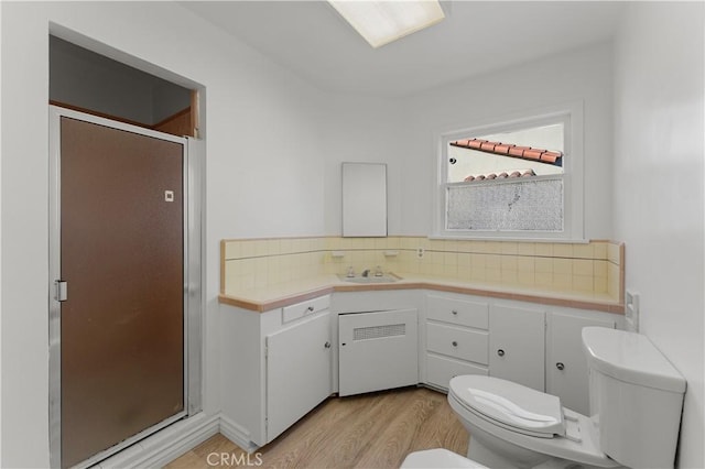 bathroom with toilet, decorative backsplash, a shower with door, and hardwood / wood-style floors