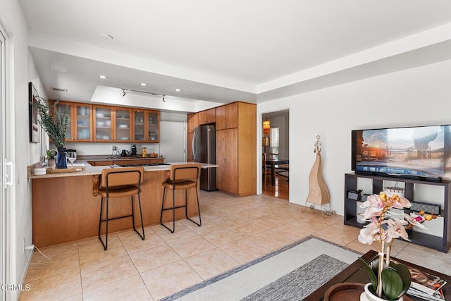 kitchen featuring light tile patterned floors, kitchen peninsula, stainless steel fridge, and a kitchen breakfast bar