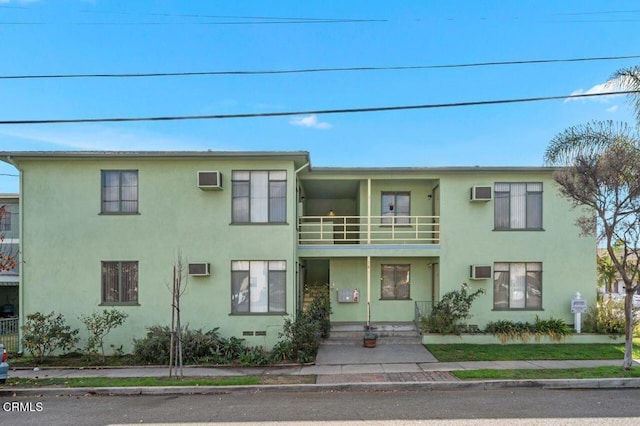 view of front of home featuring a wall mounted AC and a balcony