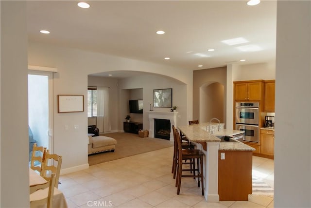 kitchen with sink, a breakfast bar area, light stone counters, a center island with sink, and stainless steel double oven