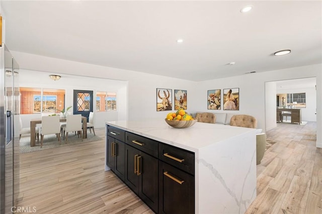 kitchen with stainless steel refrigerator with ice dispenser, a kitchen island, light stone counters, and light hardwood / wood-style flooring