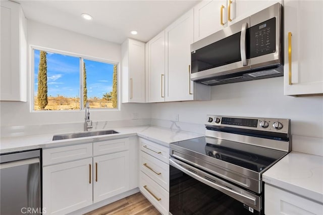 kitchen featuring white cabinetry, sink, stainless steel appliances, light stone countertops, and light wood-type flooring