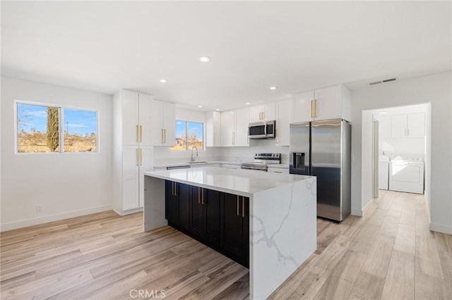 kitchen with a kitchen island, separate washer and dryer, sink, white cabinets, and stainless steel appliances