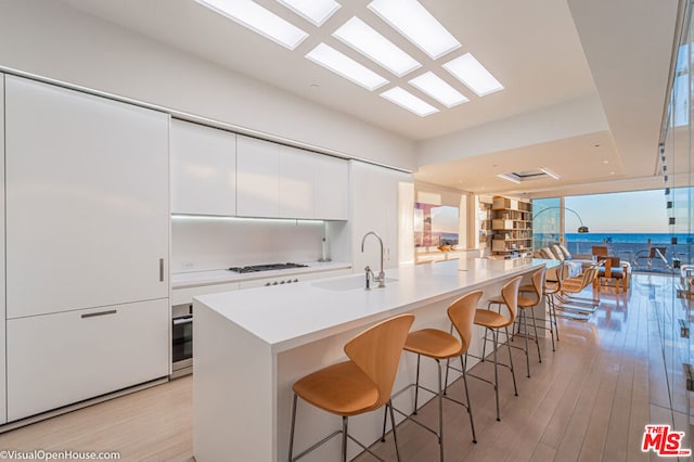 kitchen with light hardwood / wood-style floors, a breakfast bar, sink, white cabinets, and white gas stovetop