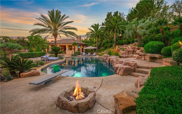 pool at dusk featuring a diving board, a patio area, and a fire pit