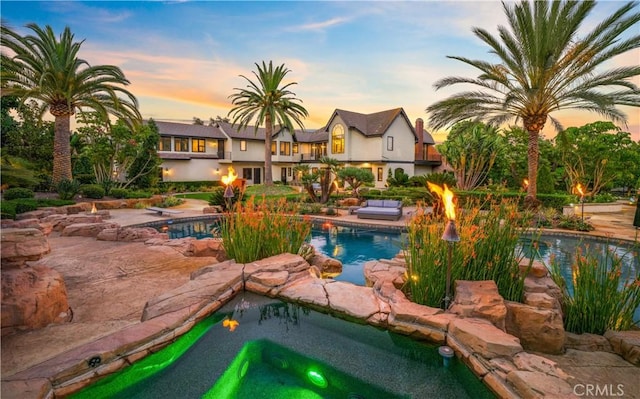 pool at dusk featuring a hot tub