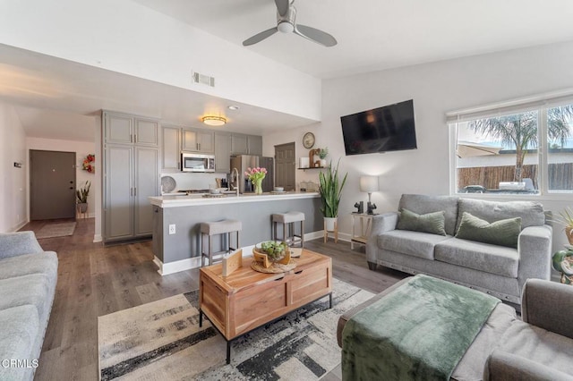 living room with a ceiling fan, visible vents, wood finished floors, and lofted ceiling