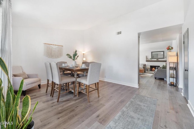 dining area with visible vents, light wood-style flooring, baseboards, and a lit fireplace