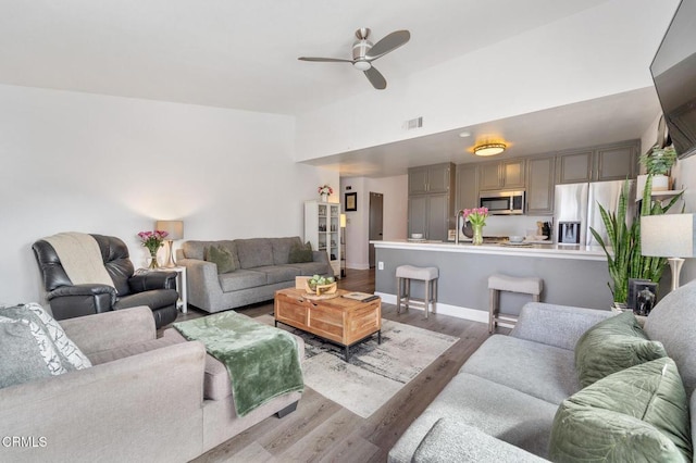 living room featuring ceiling fan, high vaulted ceiling, baseboards, wood finished floors, and visible vents
