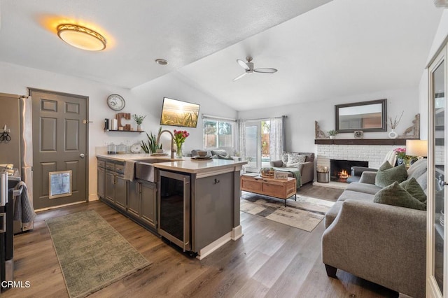 kitchen with a ceiling fan, a brick fireplace, a sink, light countertops, and beverage cooler