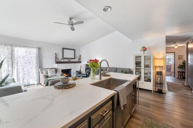 kitchen with a fireplace, open floor plan, ceiling fan, a sink, and dark wood finished floors