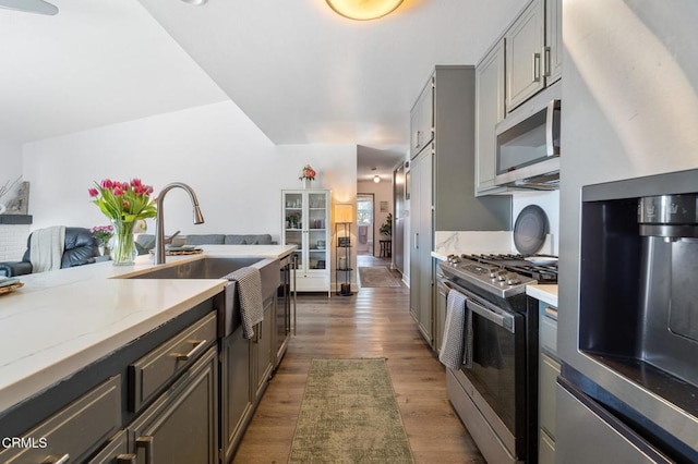 kitchen with light stone counters, a sink, dark wood finished floors, stainless steel appliances, and gray cabinetry