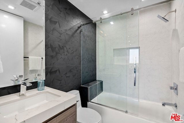 full bathroom with combined bath / shower with glass door, vanity, tile walls, and toilet