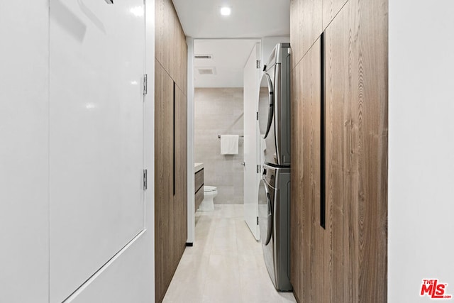 washroom with stacked washing maching and dryer, light tile patterned flooring, and tile walls