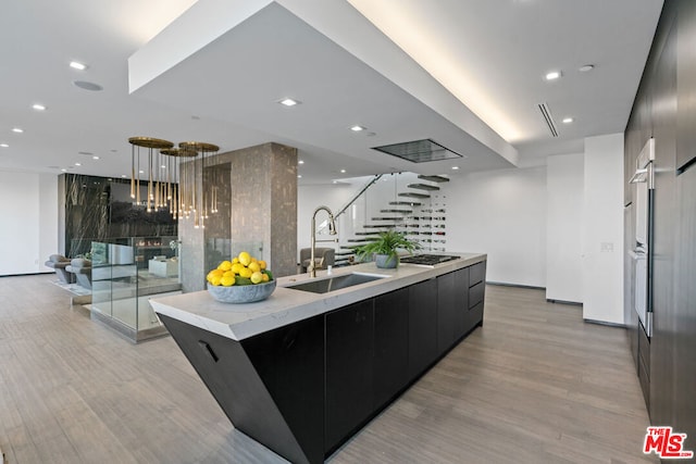 kitchen with light wood-type flooring, hanging light fixtures, a spacious island, and sink