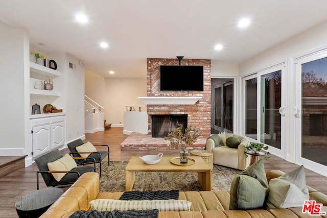 living room featuring a brick fireplace, built in features, and wood-type flooring