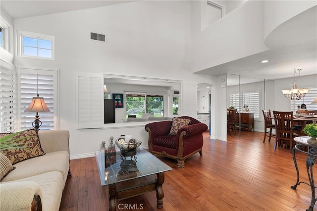 living room with high vaulted ceiling, wood-type flooring, and a notable chandelier