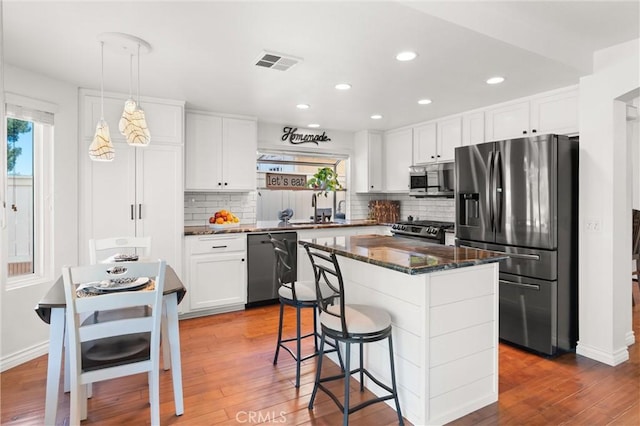 kitchen featuring white cabinets, a center island, decorative light fixtures, stainless steel appliances, and sink