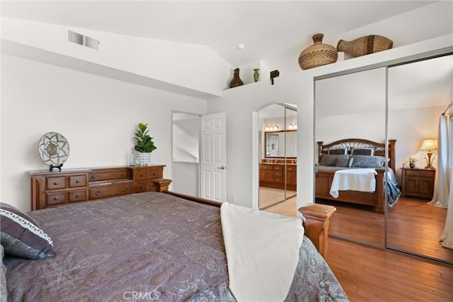 bedroom with lofted ceiling, ensuite bath, a closet, and hardwood / wood-style flooring