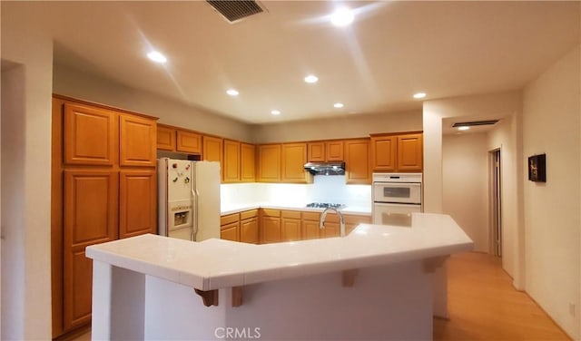 kitchen featuring a kitchen breakfast bar, white appliances, a center island with sink, and light hardwood / wood-style flooring