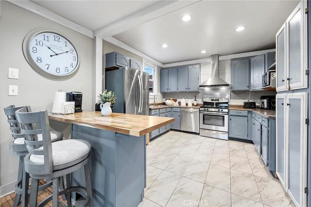 kitchen with butcher block countertops, stainless steel appliances, a kitchen breakfast bar, wall chimney range hood, and crown molding