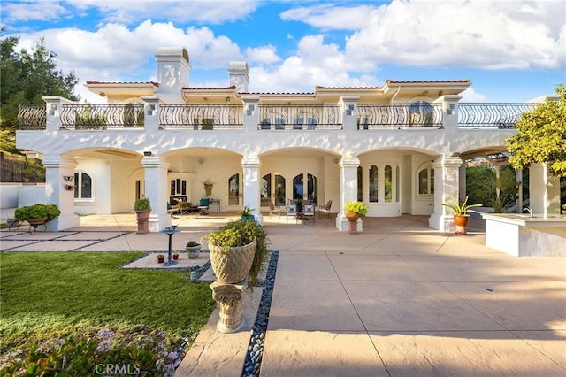 rear view of house with a yard, a balcony, and a patio