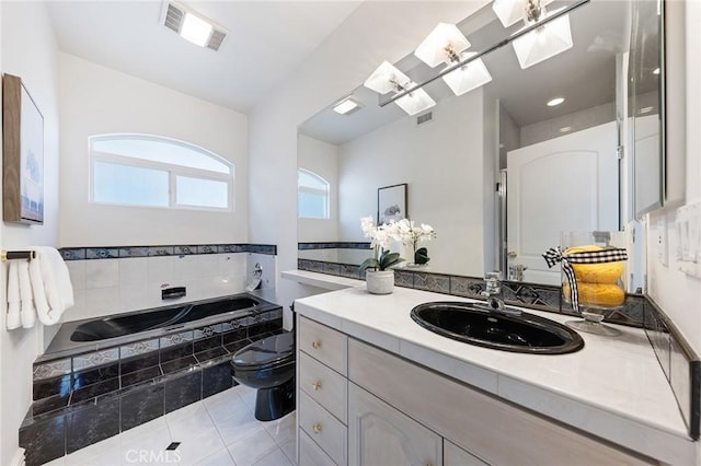 bathroom with tile patterned floors, vanity, a skylight, toilet, and a relaxing tiled tub