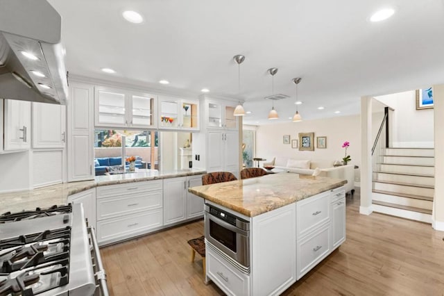 kitchen with white cabinetry, hanging light fixtures, stainless steel appliances, a center island, and island range hood