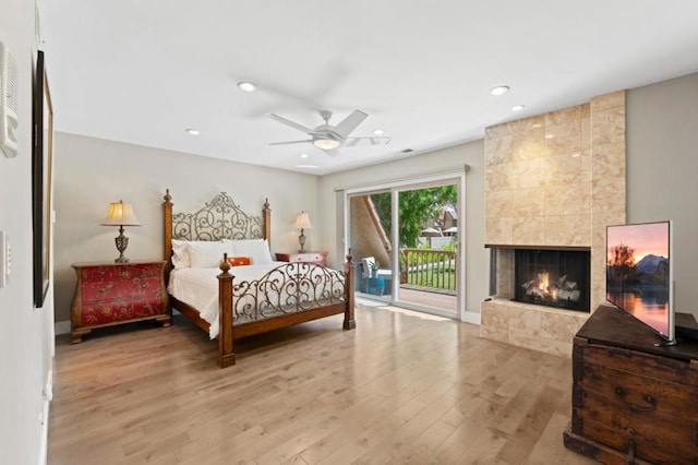 bedroom with access to exterior, a tile fireplace, ceiling fan, and light wood-type flooring