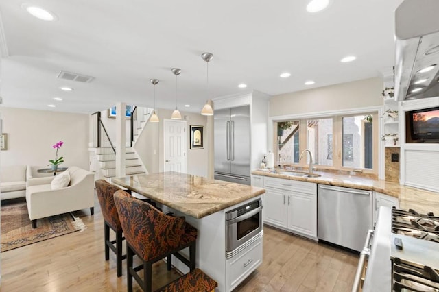 kitchen with appliances with stainless steel finishes, pendant lighting, sink, a breakfast bar area, and white cabinets