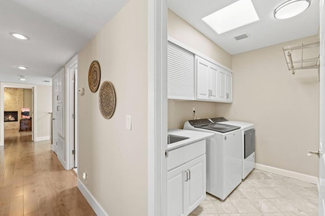 clothes washing area featuring cabinets, light wood-type flooring, washer and clothes dryer, and a skylight