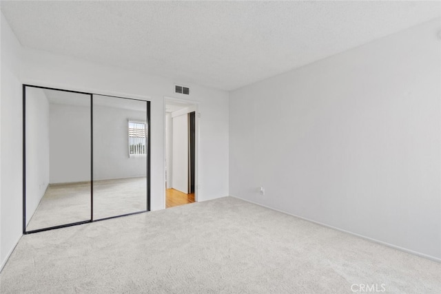 unfurnished bedroom with light carpet, a textured ceiling, and a closet