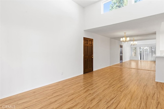 spare room featuring a chandelier, a high ceiling, and light wood-type flooring