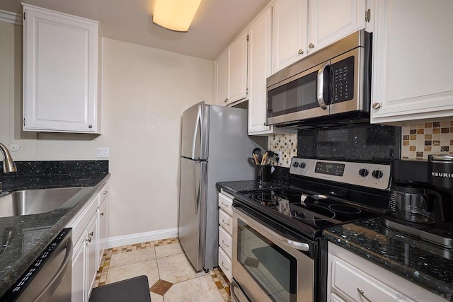 kitchen featuring light tile patterned floors, stainless steel appliances, dark stone counters, white cabinets, and sink