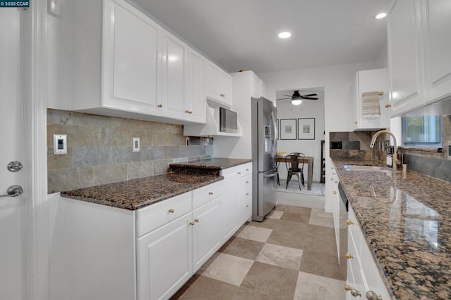 kitchen with stainless steel fridge, ceiling fan, dark stone counters, white cabinets, and sink