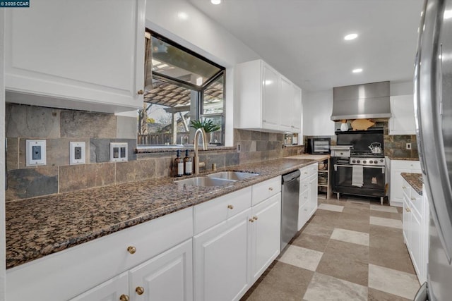 kitchen featuring wall chimney range hood, sink, appliances with stainless steel finishes, white cabinets, and dark stone counters