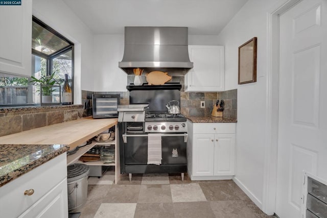 kitchen featuring extractor fan, stainless steel range with gas cooktop, decorative backsplash, dark stone countertops, and white cabinets