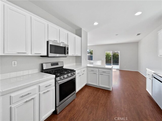 kitchen with appliances with stainless steel finishes, white cabinetry, dark hardwood / wood-style floors, tile counters, and kitchen peninsula