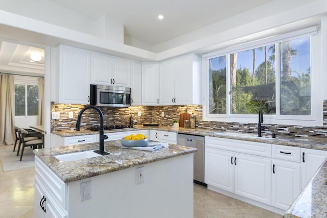 kitchen featuring sink, white cabinetry, a center island with sink, appliances with stainless steel finishes, and light stone countertops