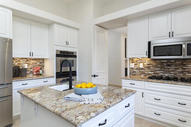 kitchen featuring white cabinetry, tasteful backsplash, stainless steel appliances, and an island with sink