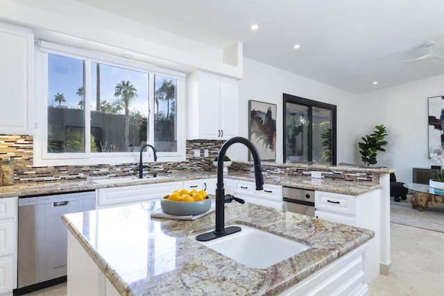 kitchen with dishwasher, a center island with sink, white cabinets, and light stone counters