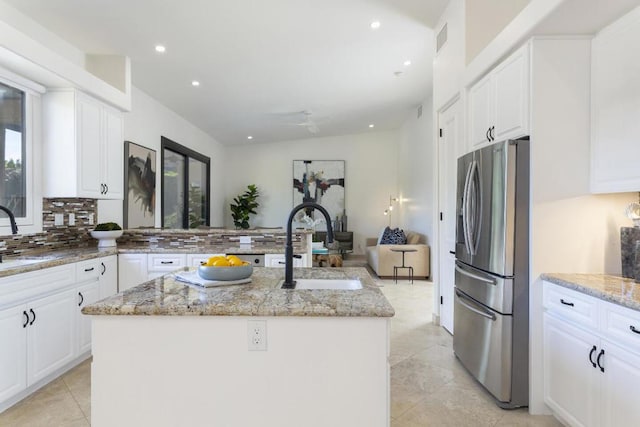 kitchen with stainless steel refrigerator with ice dispenser, an island with sink, light stone counters, and white cabinets