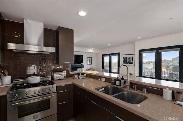 kitchen with sink, light stone counters, stainless steel range, decorative backsplash, and wall chimney exhaust hood