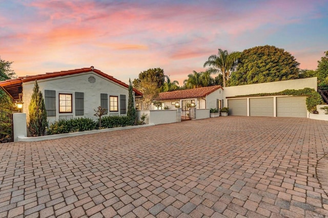 mediterranean / spanish-style house with a fenced front yard, an attached garage, decorative driveway, a gate, and stucco siding