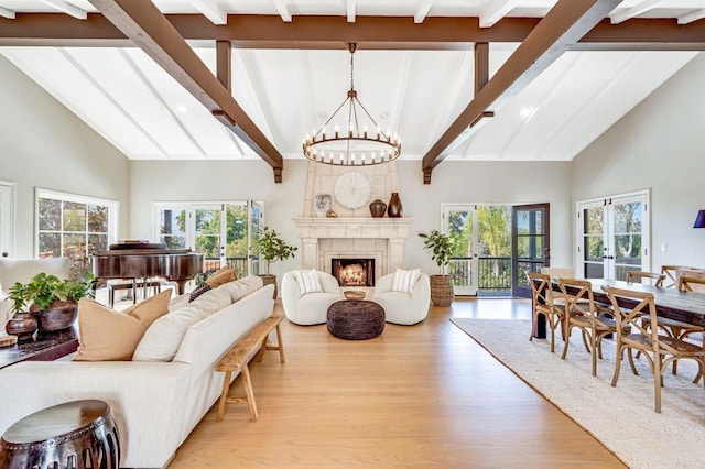 living room featuring a healthy amount of sunlight, a warm lit fireplace, light wood-type flooring, and a notable chandelier